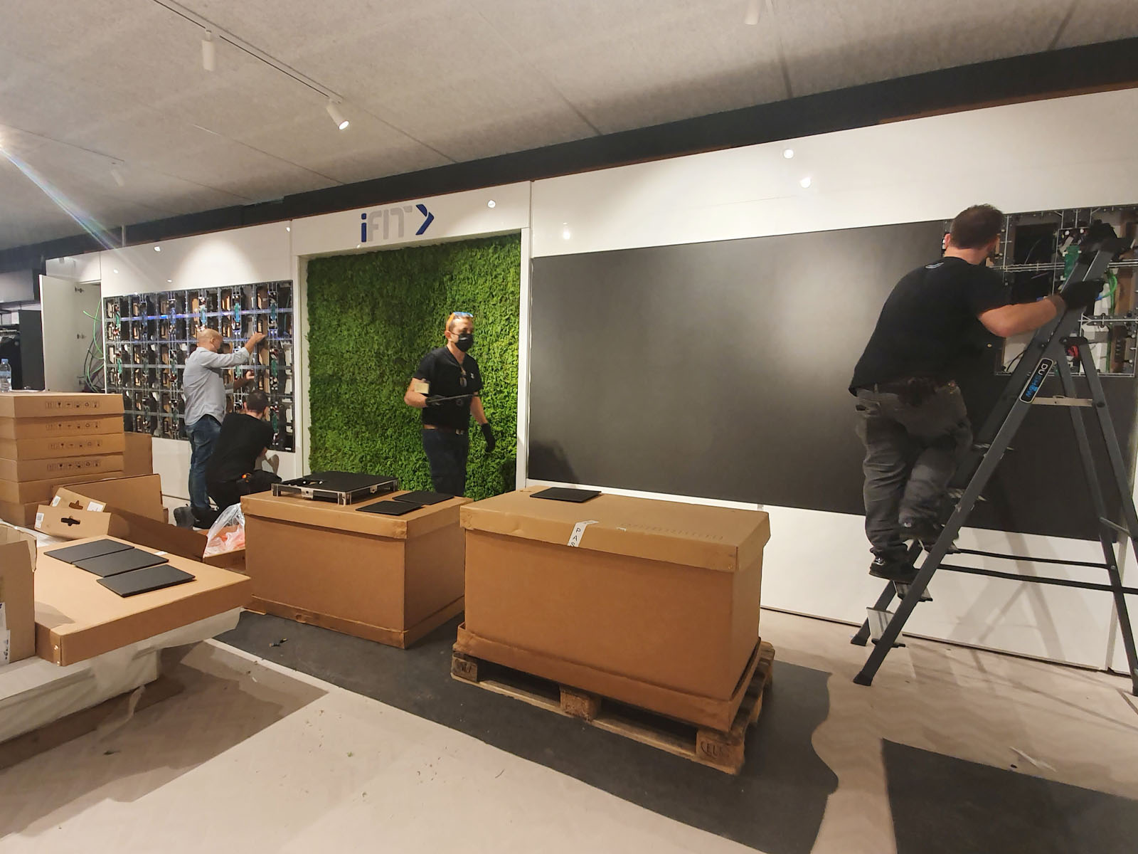 Installation d’un stand d’exposition iFIT avec équipements sportifs, écrans et éléments scénographiques en cours de montage.